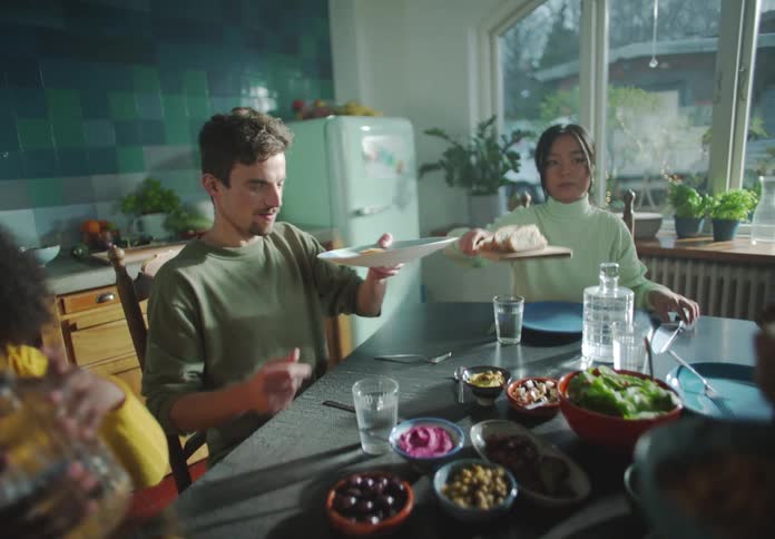 Friends sit around table in kitchen passing and serving food
