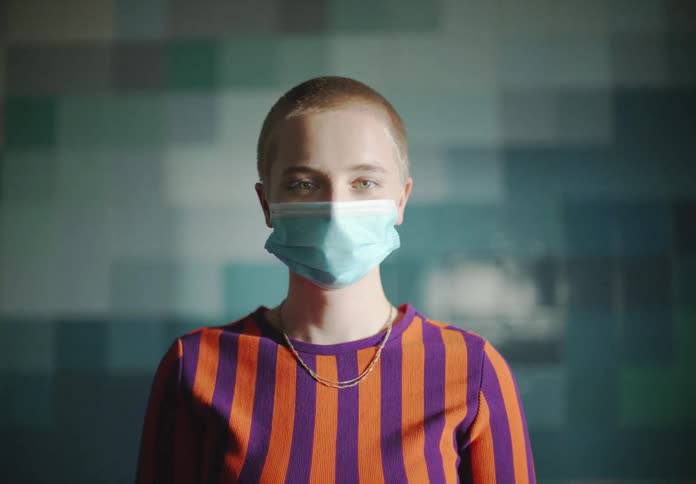 Woman with a buzz cut smiling while posing with a facial mask on