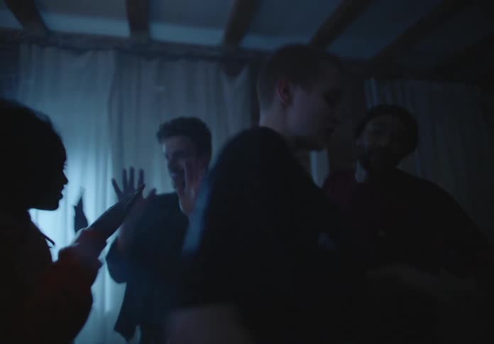 A group of friends dance in an apartment under strobing lights