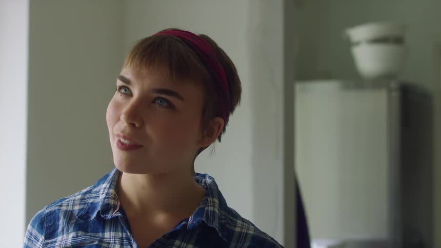 Woman with brown short hair blue eyes and plaid shirt paints wall and looking at it smiling in room at home