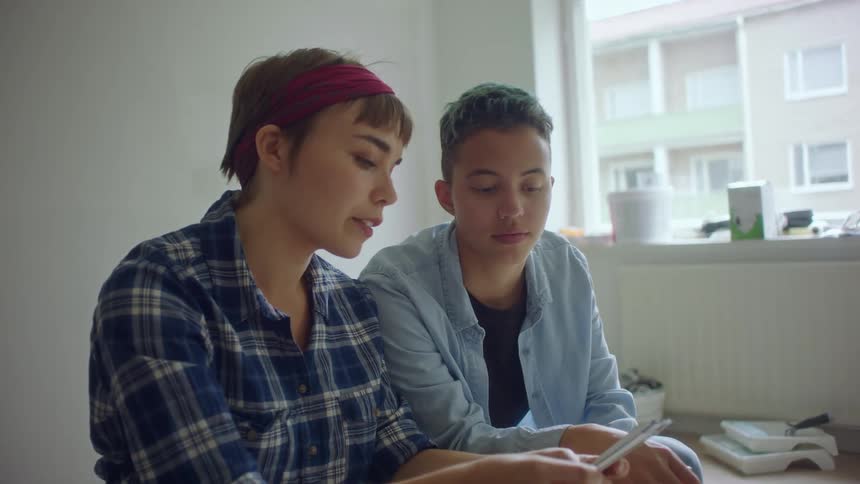 Two women sit in a home and look at paint samples