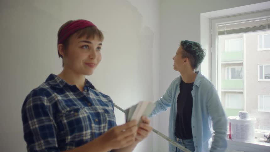 A woman paints while another checks colors on cards