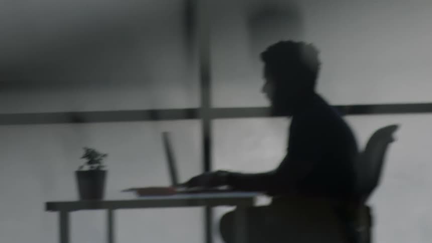 The silhouette of a man typing on a laptop