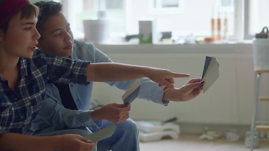 Two people sit in room under remodel contemplating paint samples