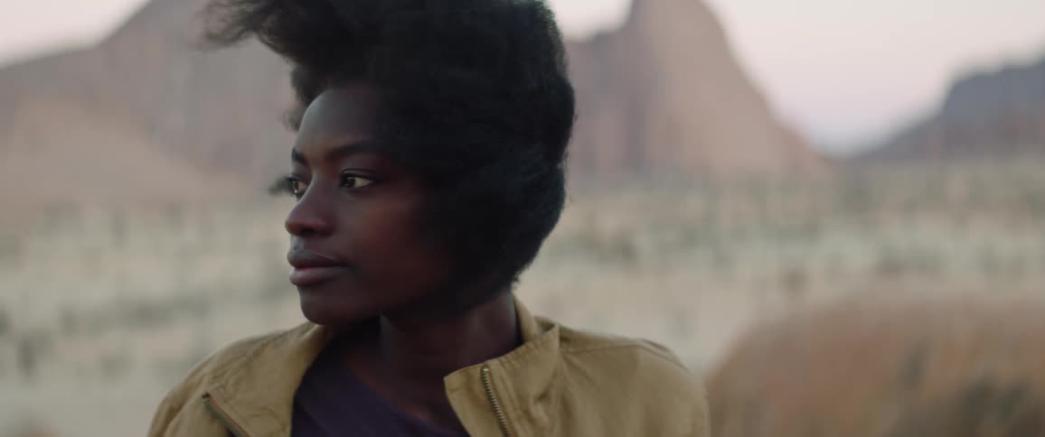 Wind blows through a womans hair as she sits in a desert during the day
