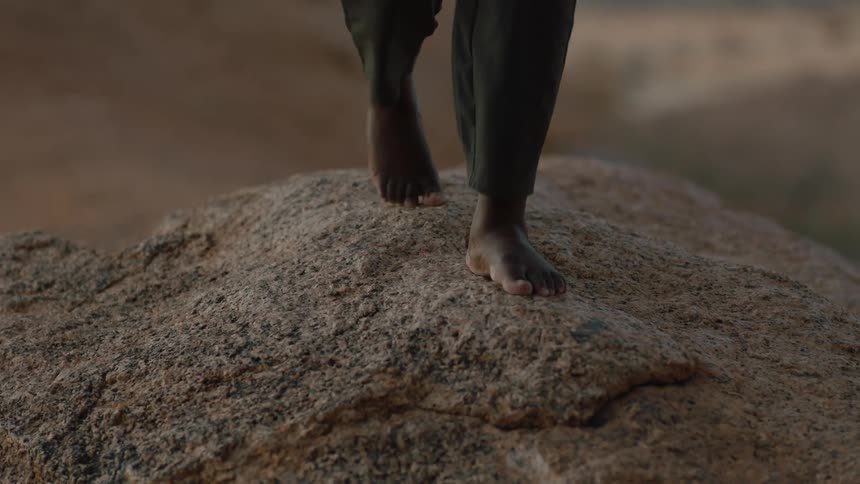 Close up of bare feet walking across a large rock on a windy day