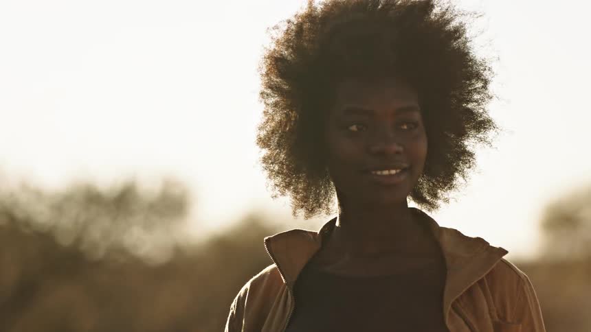 Woman with afro walks and smiles at camera in field