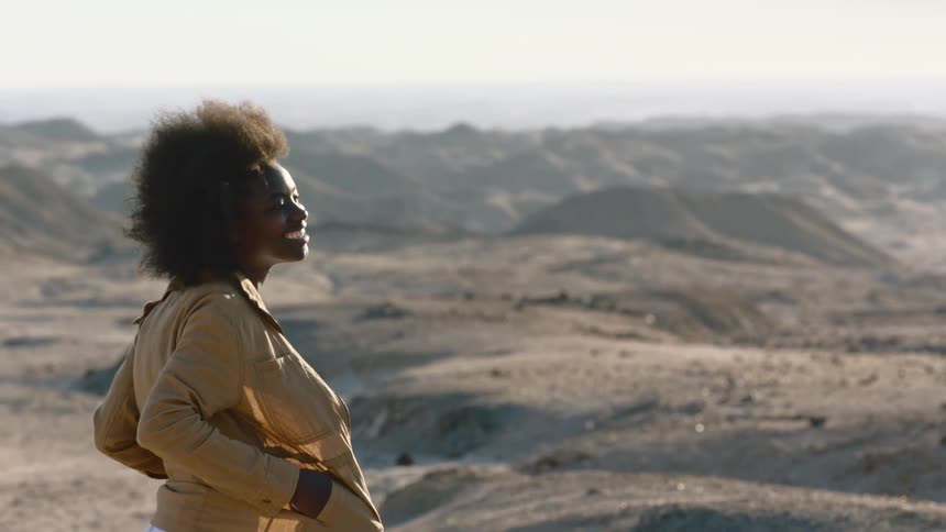 Wind blowing the hair of a young happy smiling woman standing near the desert hills