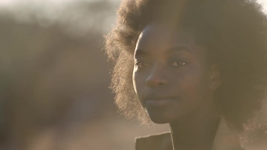Young woman standing in the wind outdoors turns to look into the camera