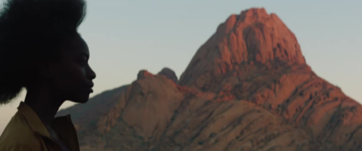 A black woman is looking at mountains as the wind blows her hair back