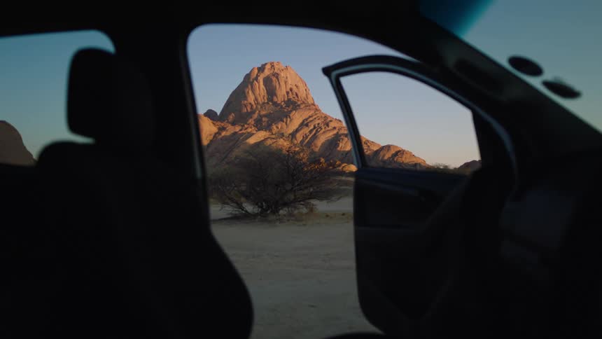 Open car door shows desert and rocky mountain under a clear sky