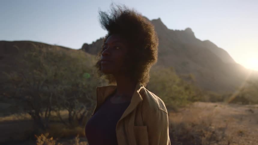 A young black woman with afro takes in the desert landscape with the wind blowing at her back