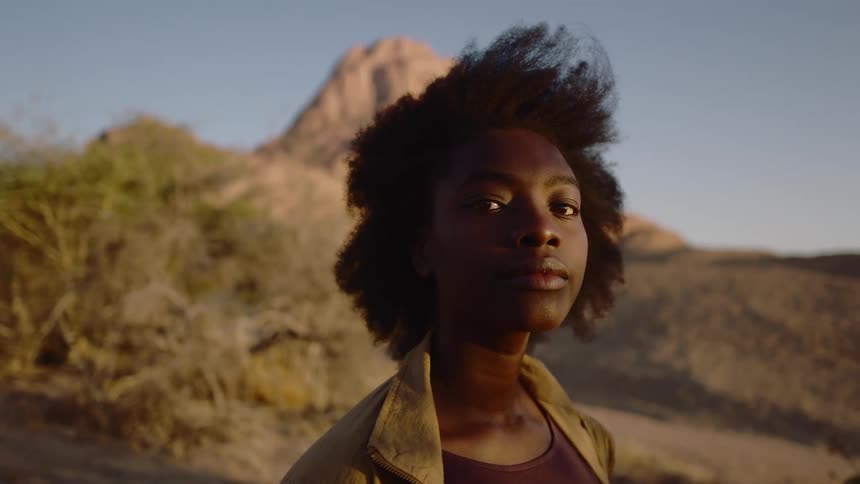 Woman with afro faces the camera and makes eye contact in the desert