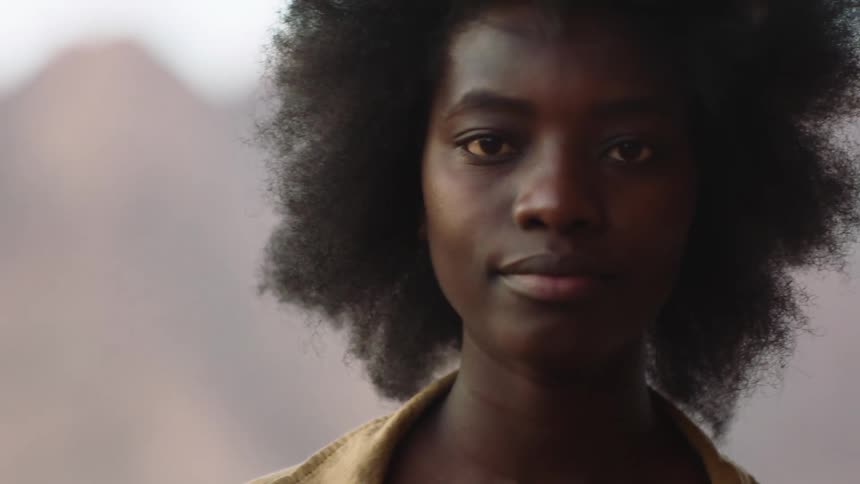 Young black woman with afro outdoors in desert looking into the camera