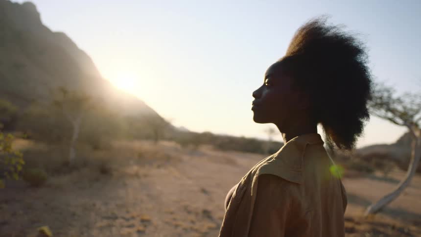 A young black woman with afro turns and looks into the camera in the desert