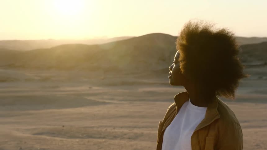 Young black female walking and staring into the desert at sunset