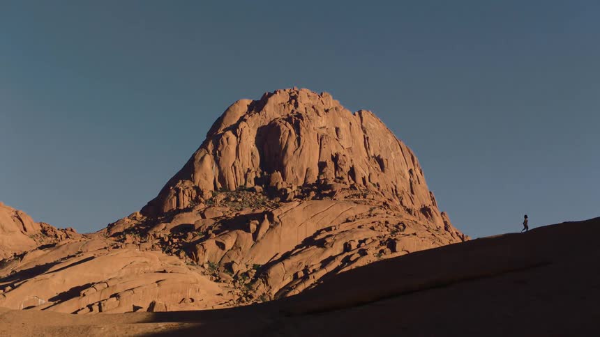 Silhouette of a person walking near a mountain under a clear sky