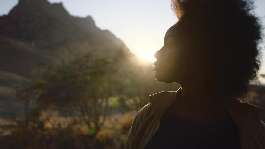 A young black woman with afro takes in the desert landscape with the wind blowing in her face