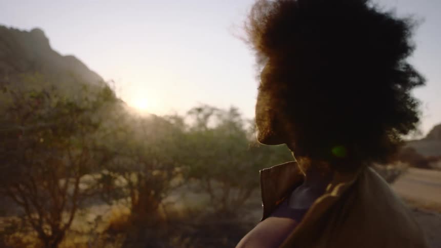 Sun shining on a woman's face as she looks at desert landscape around her at dusk