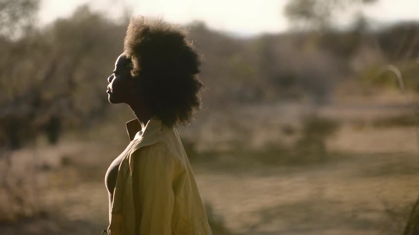 A pensive woman stands and looks out at the desert landscape