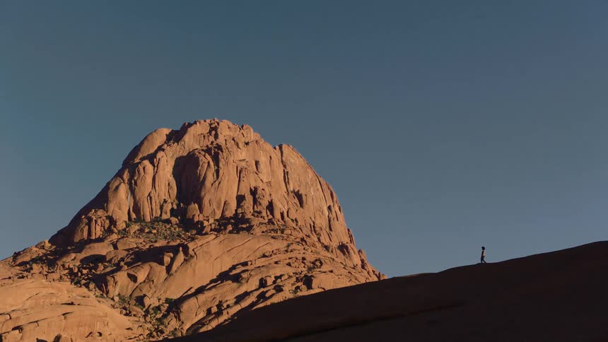 Silhouette of a person walking near a mountain under a clear sky
