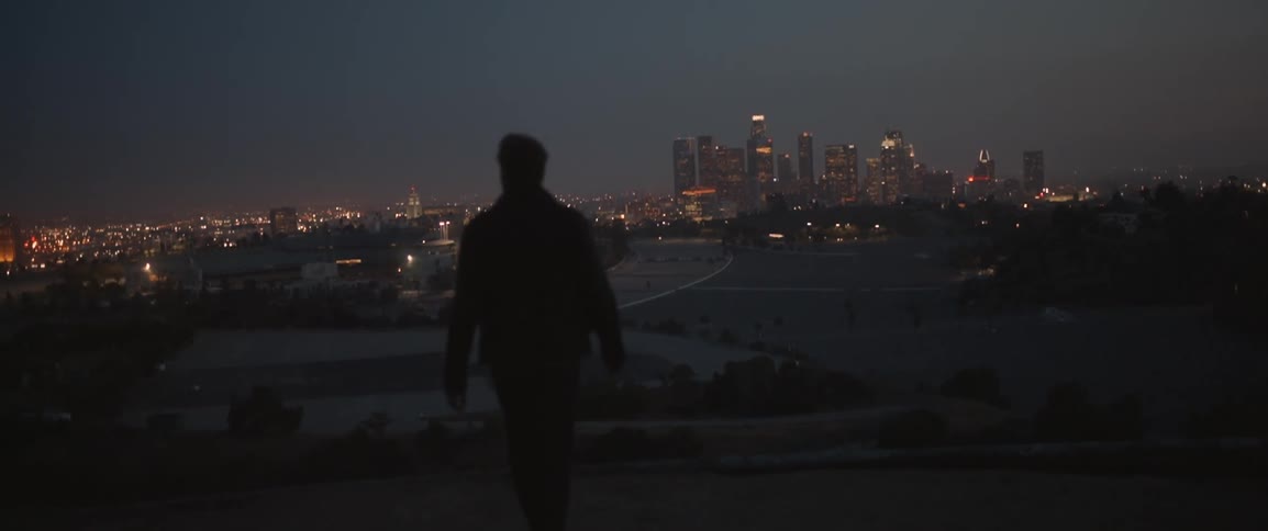 A man walks on a hill overseeing a city at dawn