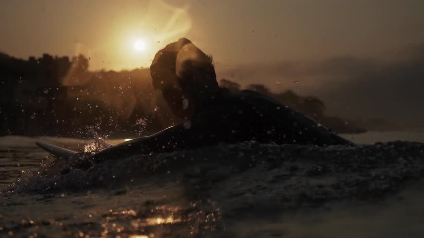 A man is surfing in the water at sunset