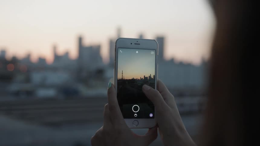 A person takes a picture of a skyline at sunset