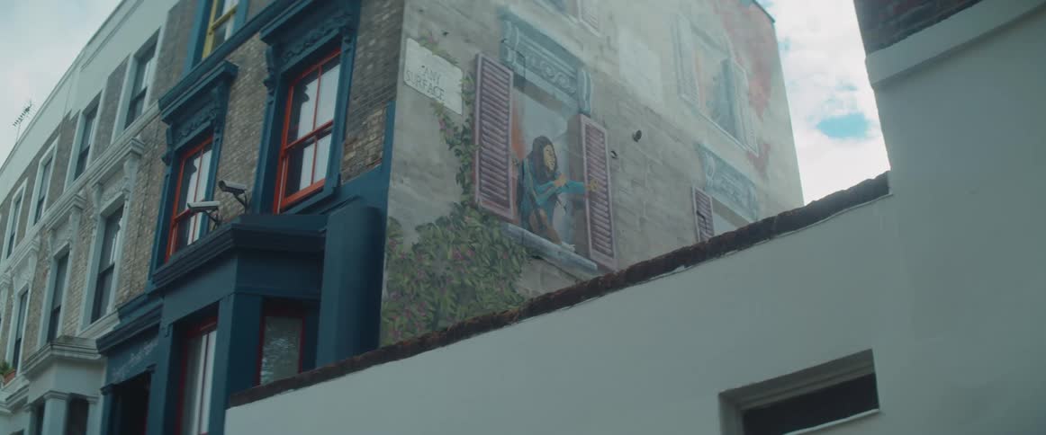 A mural painting on the side of an apartment building of a woman sitting in a window sill