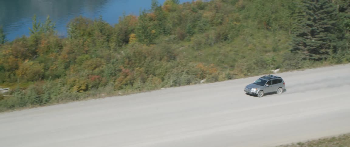 A vehicle travels along a dusty road through a forest