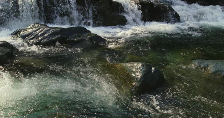Water is flowing over rocks and boulders and swirling in the rapids of a river