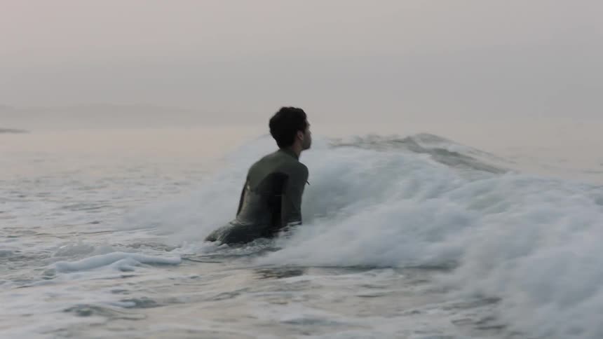 A man moves into the rough waters with his surfboard