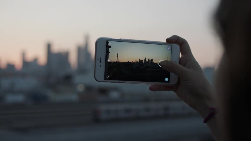 A person is using a phone to take photos of a city in the distance