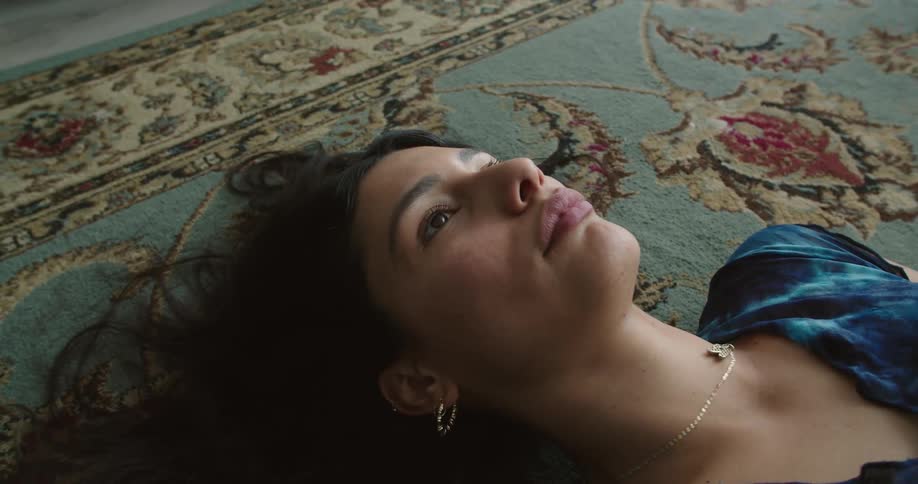 A woman lies on a rug at home and stares at the ceiling