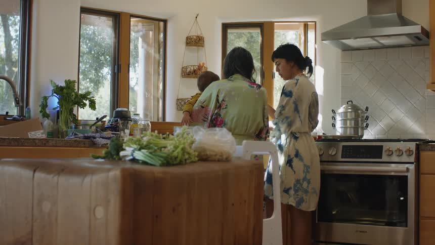 Grandma holds the baby in the kitchen while her daughter talks to her