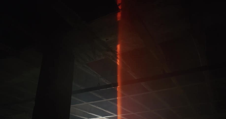 Laser beam cross large dark room near ceiling crossing a exposed pipe