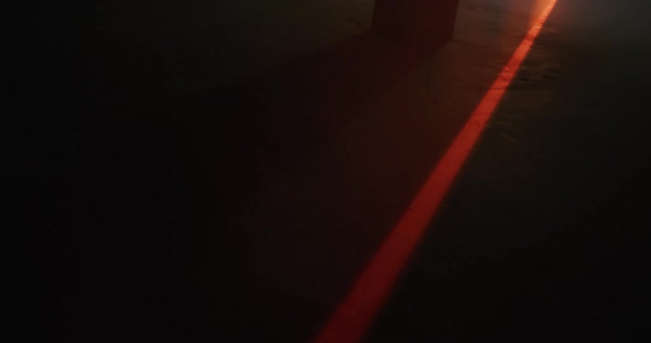 A red beam of light travels across the ground passing a column
