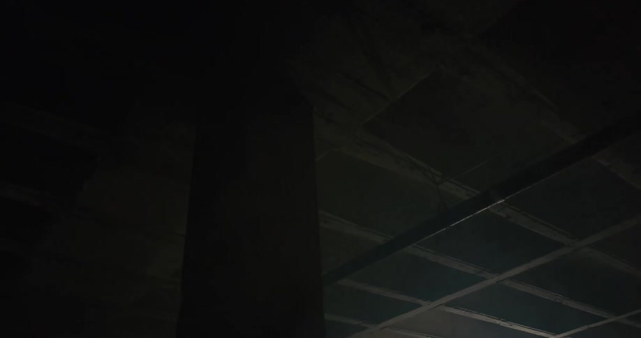 A red laser beam shines across a ceiling with pipes and joists