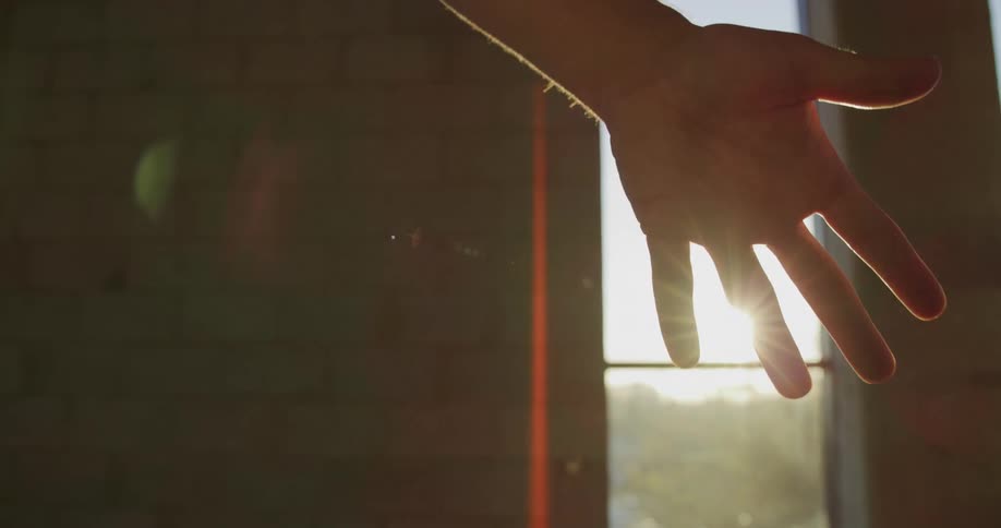 A person is waving their hand in front of the sun shining in the window