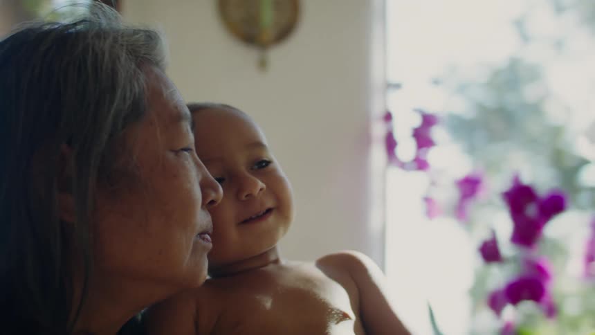 Grandma smiles as she holds a happy baby who high fives his mom
