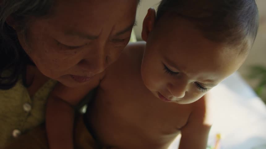 Grandmother holding her grandson on her arms over the bed at home