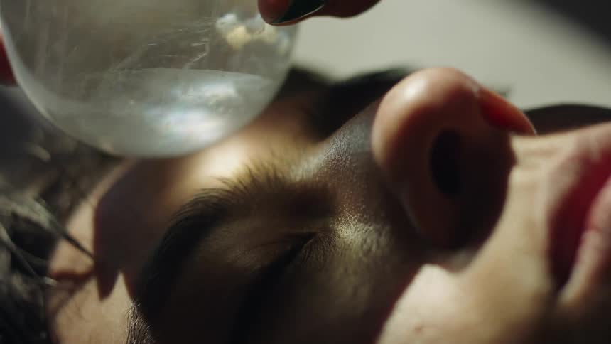 Close up of a woman lying down rolling a small crystal ball on her face