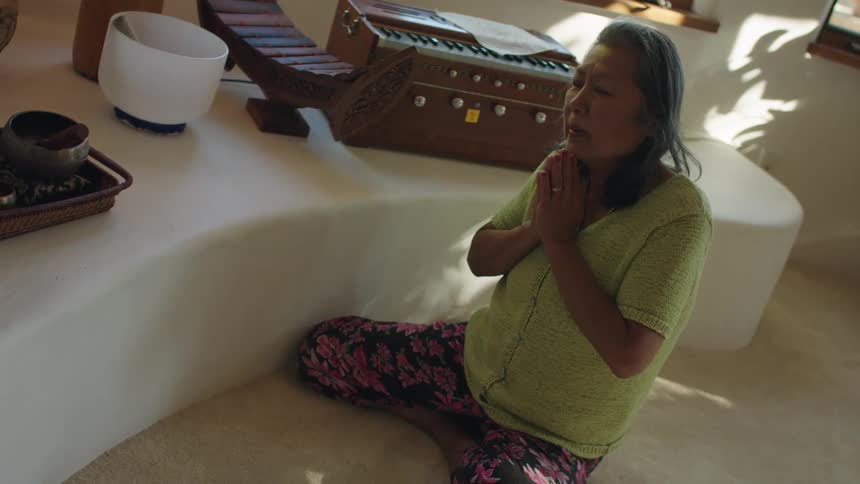 An elderly woman sits on the floor at home and prays