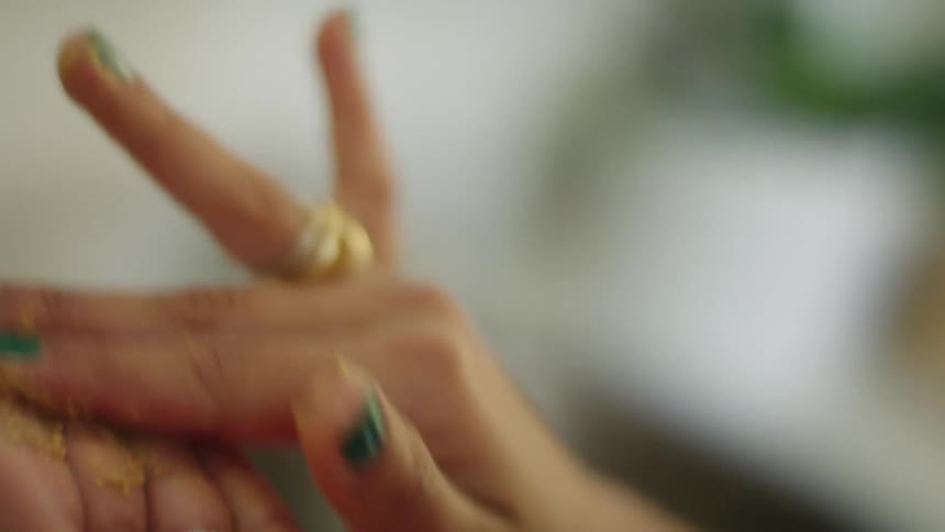 Woman picks mixture from small bowl sitting on tiled surface and rubs it between fingers