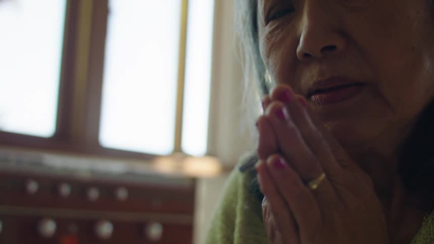 An elderly woman is praying as she kneels