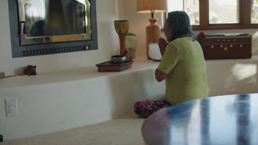 An elderly woman sits at home and prays