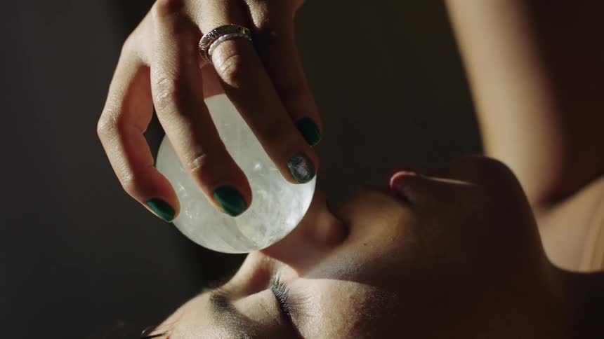 Young woman rolling a quartz ball gently over her face inside a dimly lit room