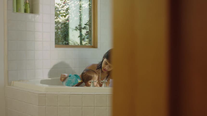 A young mother is in the bathtub bathing her baby