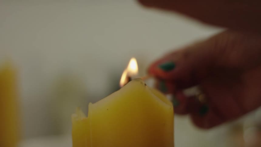 A woman lights a match and then uses it to light a candle