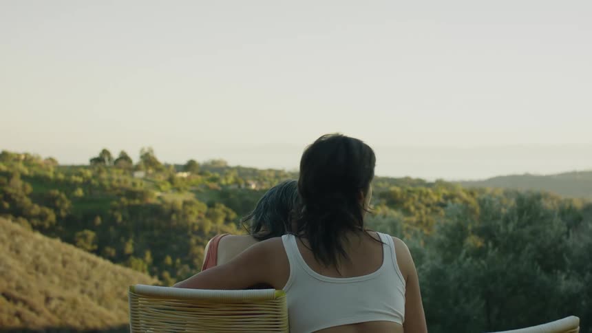 A young woman rubbing her grandmothers back outside overlooking a valley